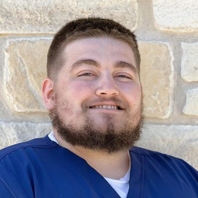 Dr. Colton Wostenberg smiling in front of a stone wall.
