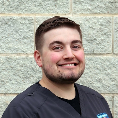 Colton Drew smiling in front of a brick wall.